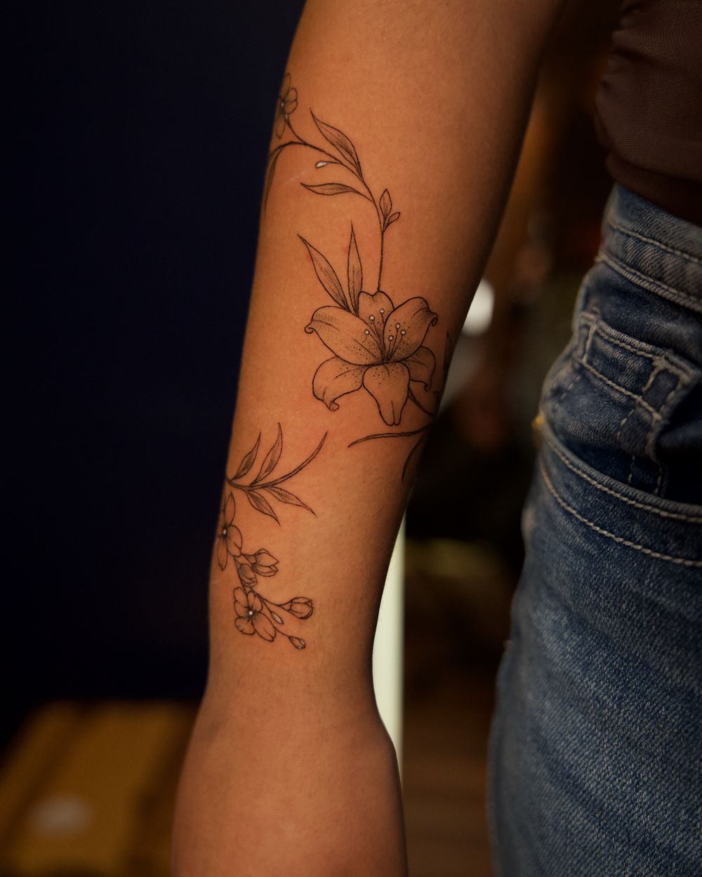 Fine-line botanical tattoo of lilies and wildflowers along the forearm, by Rodney Alacan