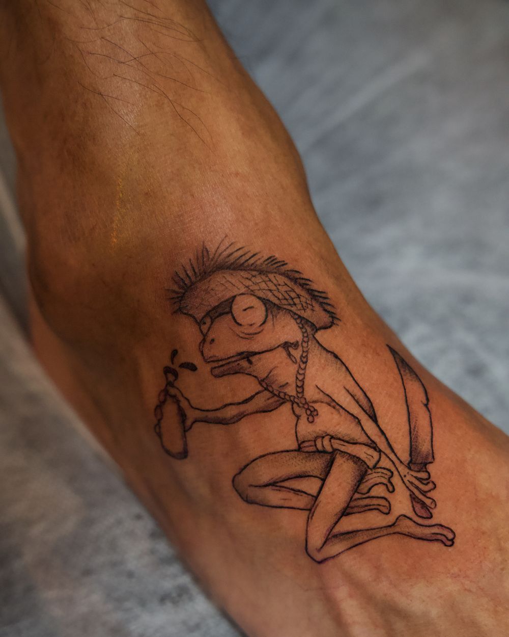 Fine-line tattoo of a coquí frog wearing a jíbaro straw hat with a machete, by Rodney Alacan